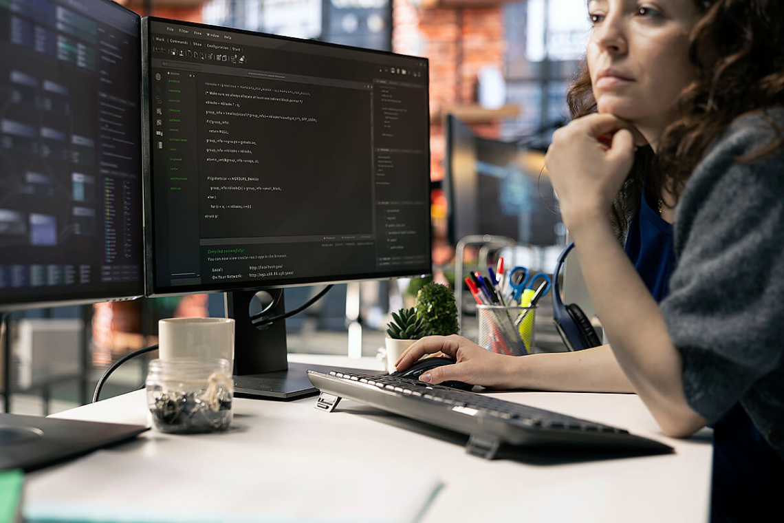 Profesional trabajando en un puesto informático con doble monitor y herramientas de gestión tecnológica.